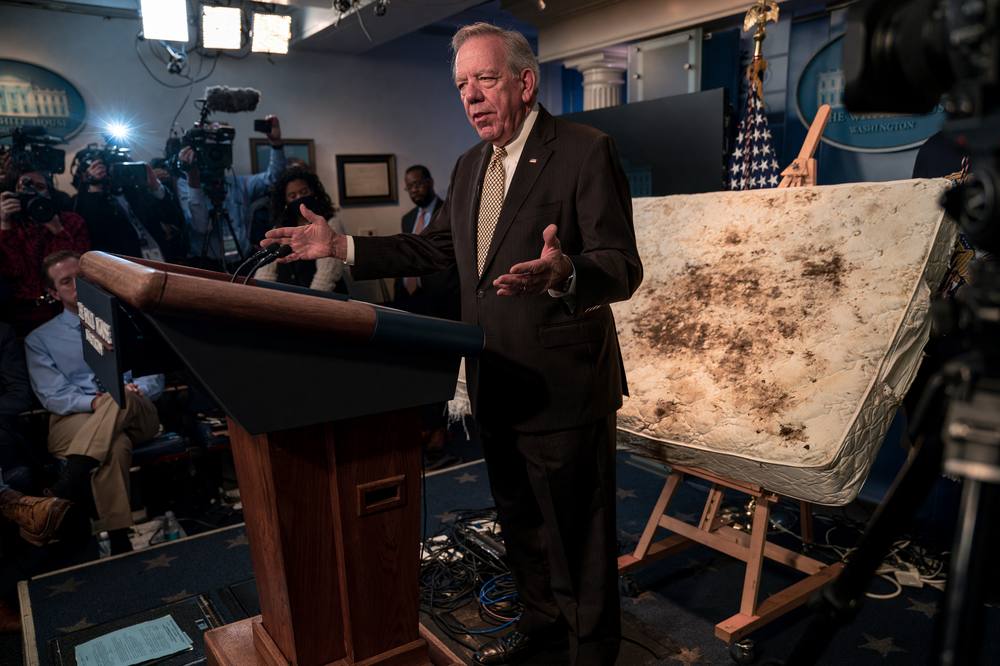A federal briefing with a stained mattress displayed on an easel beside the podium